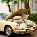 Vintage car with open hood filled with decorative pillows outdoors.